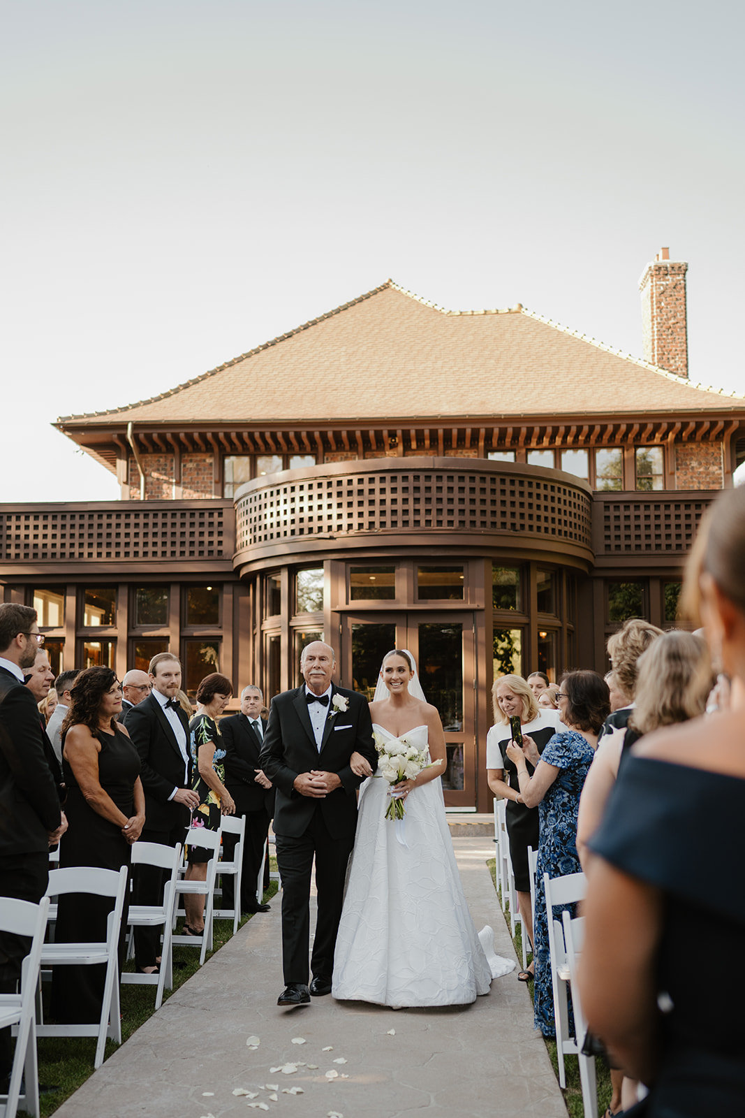 Bride and her father walking down the stone aisle under warm golden hour light during the ceremony.